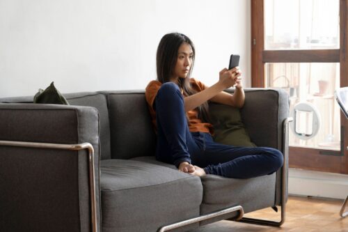stock market simulator daytrader Wide shot of woman trading from her cell phone sitting on a couch