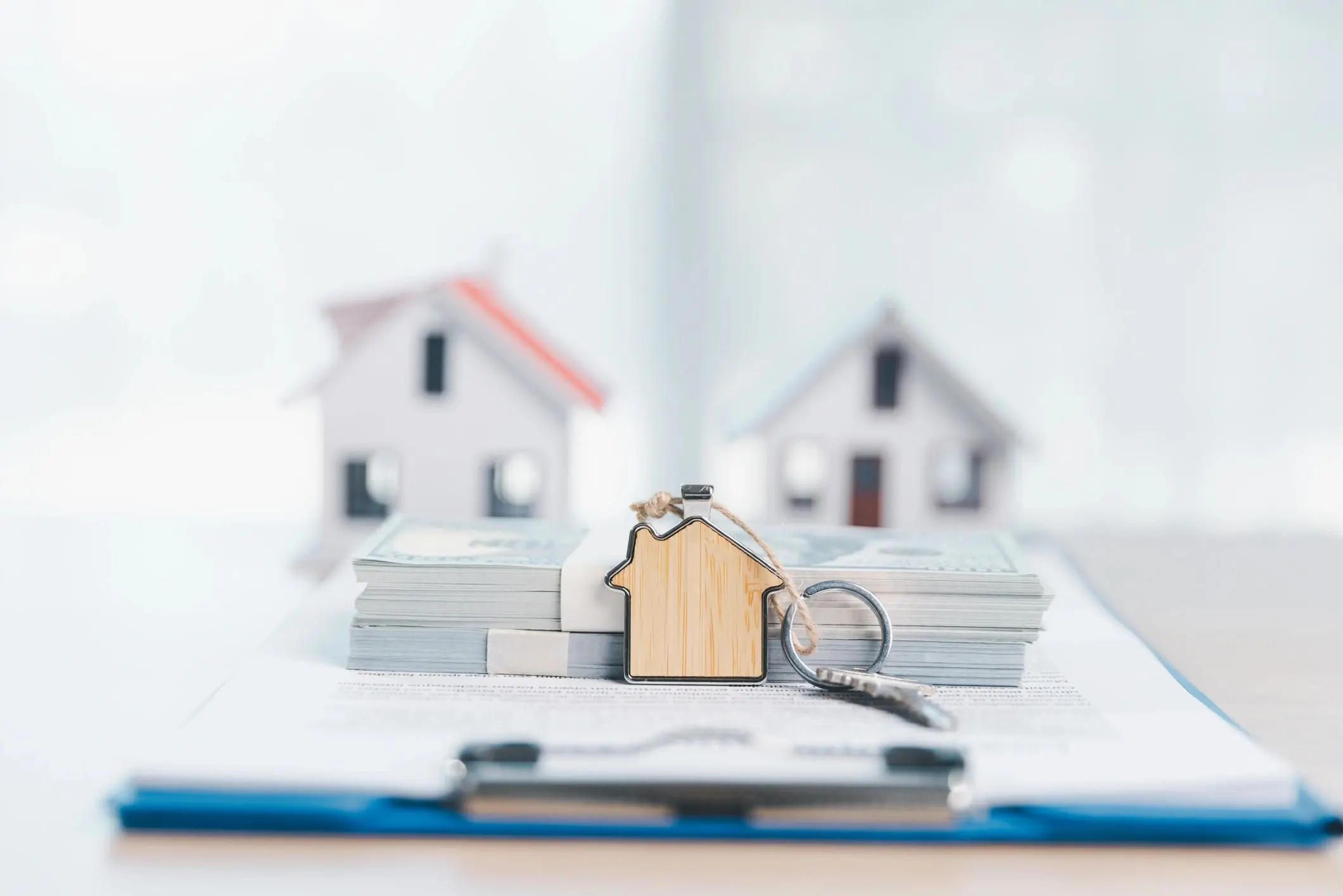House keys with a house-shaped keychain on a stack of cash and mortgage contract