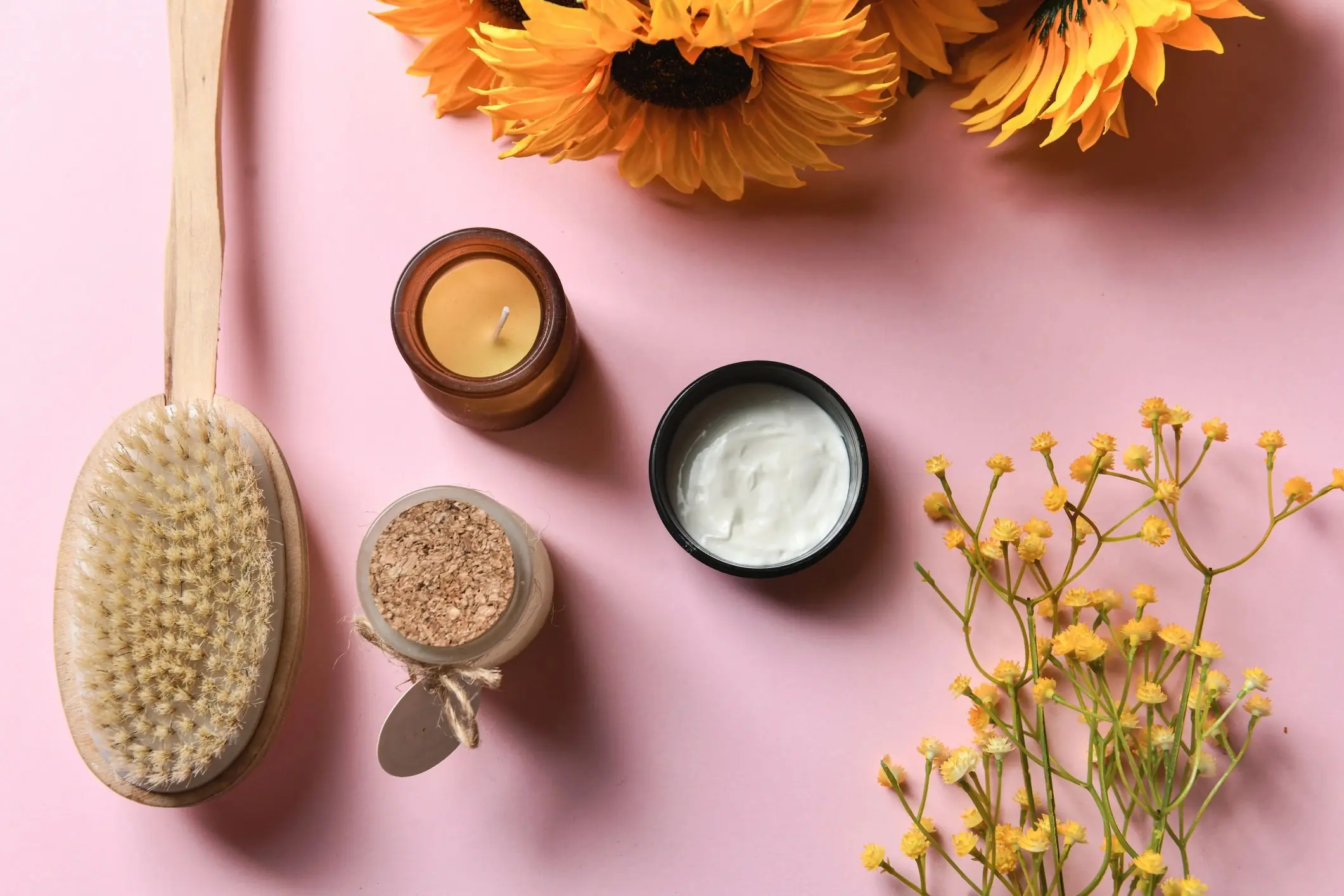 Personal care products with candles and moisturizer on a pink background